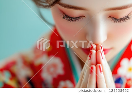 A woman wearing a red kimono praying with her hands together 125538462