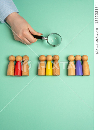The concept of market segmentation. Target audience, customer care. Market group of buyers. Customer relationship management. Businesswoman looking through a magnifying glass at figurines of people 125538584