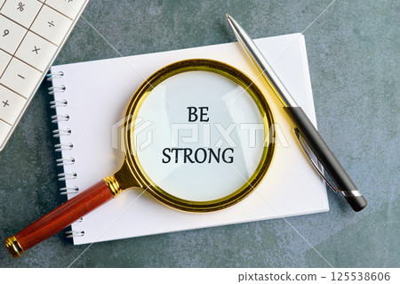 A motivational phrase encourages resilience, presented clearly under a magnifying glass on a notepad. A pen sits alongside, indicating a focused workspace during brainstorming or planning 125538606