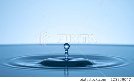 single water droplet rises above calm water surface, creating soft ripples in serene and minimalist setting. tranquil blue tones evoke sense of peace and simplicity 125539047