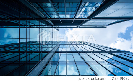 stunning view of modern skyscraper showcasing steel and glass framework, captured from dynamic perspective below. reflection of clouds adds depth and beauty to architectural design 125539052
