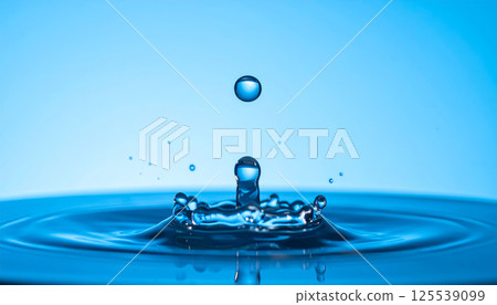 water droplet creates mesmerizing splash in crystal clear water, symbolizing purity and freshness. elegant blue tones enhance serene atmosphere of this captivating moment 125539099
