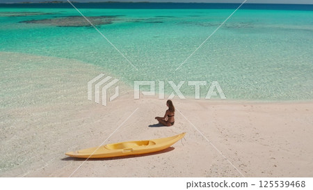 Aerial view of a serene moment on a pristine tropical beach, featuring a woman enjoying the tranquil atmosphere and a kayak resting on the soft, white sand Aerial view of a serene moment on a pristine tropical beach, featuring a woman enjoying the tranquil atmosphere and a kayak resting on the soft, white sand 125539468