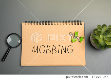 Mobbing concept. Act of bullying or harassing a person, typically in a workplace or school setting, where a group of people targets an individual with persistent mistreatment. Notepad with inscription 125541046