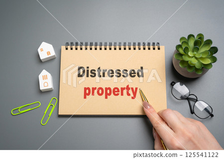 Distressed property concept. Real estate that is under financial stress usually because the owner cant keep up with mortgage payments, taxes, or upkeep. Notepad with inscription and miniature houses Distressed property concept. Real estate that is under financial stress usually because the owner cant keep up with mortgage payments, taxes, or upkeep. Notepad with inscription and miniature houses 125541122