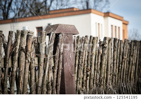 Rustic Wooden Fence with Branches and Modern Building in Background 125541195