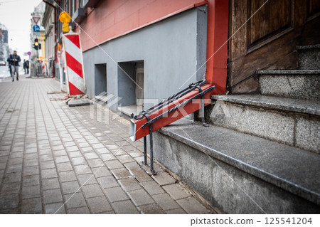 Red Drainpipe and Street Construction Barriers by Stairs with Wooden Door Red Drainpipe and Street Construction Barriers by Stairs with Wooden Door 125541204