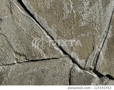Close-up view of a textured stone surface showcasing natural cracks and patterns. The uneven surface highlights the rugged beauty and organic formations of the rock. Close-up view of a textured stone surface showcasing natural cracks and patterns. The uneven surface highlights the rugged beauty and organic formations of the rock. 125541452