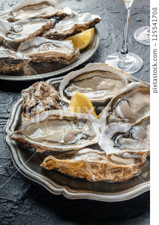 Fresh raw oysters on ice with lemon, on a black slate background Fresh raw oysters on ice with lemon, on a black slate background 125541708