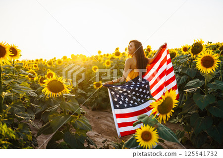 Woman proudly hold waving american USA flag in in the sunflower field. Independence Day, 4th July. 125541732