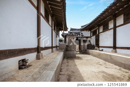 Traditional Korean hanok courtyard with white plastered walls wooden beams and a historic brick chimney structure under a clear blue sky Traditional Korean hanok courtyard with white plastered walls wooden beams and a historic brick chimney structure under a clear blue sky 125541869