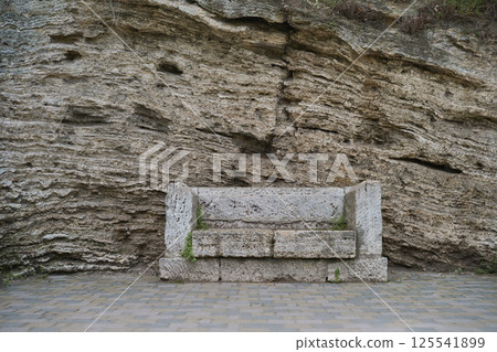 Ancient stone bench built into sandstone rock wall, textured weathered surface with green moss spots, natural minimalist landscape conveying historical atmosphere resting place Ancient stone bench built into sandstone rock wall, textured weathered surface with green moss spots, natural minimalist landscape conveying historical atmosphere resting place 125541899