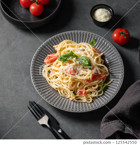 Creamy spaghetti with cherry tomatoes, parmesan cheese and basil on a plate on a dark background. 125542550