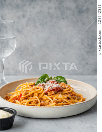 Spaghetti bolognese with tomato sauce, basil and parmesan cheese on a plate on a gray background Spaghetti bolognese with tomato sauce, basil and parmesan cheese on a plate on a gray background 125542551