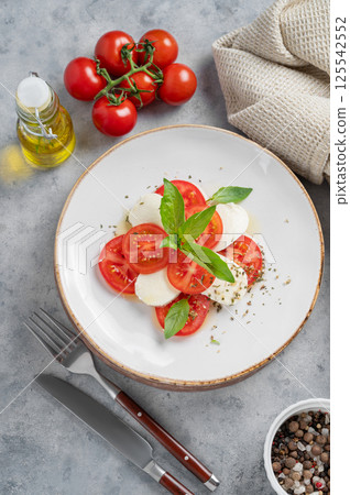 Caprese salad with sliced tomatoes, mozzarella and basil on a plate on a light background Caprese salad with sliced tomatoes, mozzarella and basil on a plate on a light background 125542552