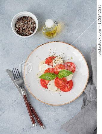 Caprese salad with sliced tomatoes, mozzarella and basil on a plate on a light background 125542553