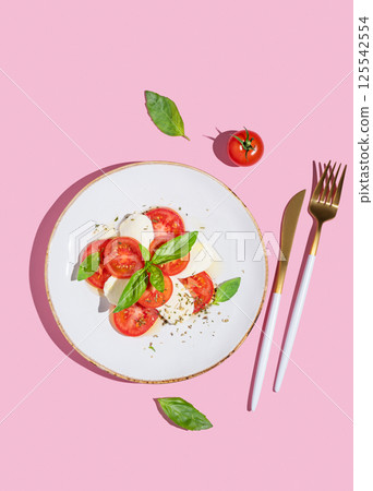 Caprese salad with fresh tomatoes, mozzarella and basil on pink background. 125542554