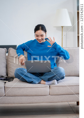 Happy woman having fun doing video call using mobile phone and Laptop sitting on sofa, home office workplace lifestyle people. 125542611