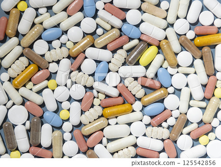 Pile of mixed white, yellow and blue medical capsules and pills on blue top view 125542856