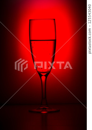 The photo has a red background and a long-stemmed glass of water in the photo. A glass of water. 125543040