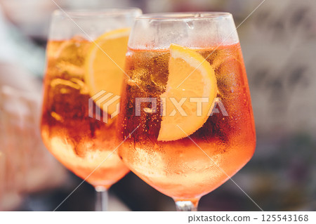 Glass of ice cold Aperol spritz cocktail served in a wine glass, decorated with slices of orange. Aperitif in street caffe Glass of ice cold Aperol spritz cocktail served in a wine glass, decorated with slices of orange. Aperitif in street caffe 125543168