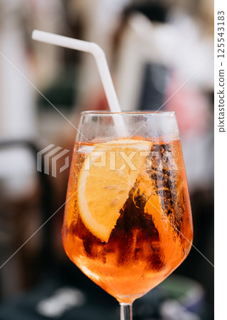 Glass of ice cold Aperol spritz cocktail served in a wine glass, decorated with slices of orange. Aperitive in street caffe in Italy 125543183