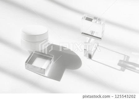 White cream cosmetic jar on acrylic geometric pedestal podium block, beauty product packaging with shadows, high angle view. Creme lotion pot cosmetics showcase presentation White cream cosmetic jar on acrylic geometric pedestal podium block, beauty product packaging with shadows, high angle view. Creme lotion pot cosmetics showcase presentation 125543202