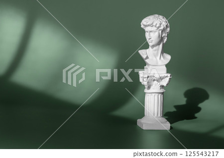 White marble head of young man, head of famous statue by Michelangelo. Gypsum copy of ancient statue head on green background with light and shadow White marble head of young man, head of famous statue by Michelangelo. Gypsum copy of ancient statue head on green background with light and shadow 125543217