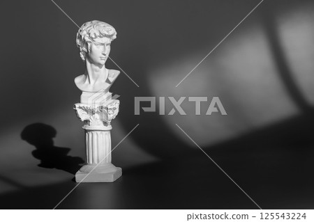 White marble head of young man, head of famous statue. Gypsum copy of ancient statue head on purple background with light and shadow 125543224