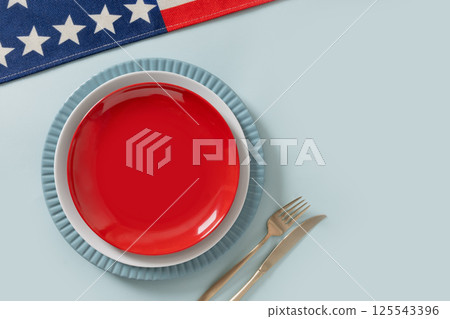 American table setting for USA Independence Day. Festive dinner with empty white plate and decoration in USA national flag colors red and blue. View from above. Copy space. American table setting for USA Independence Day. Festive dinner with empty white plate and decoration in USA national flag colors red and blue. View from above. Copy space. 125543396