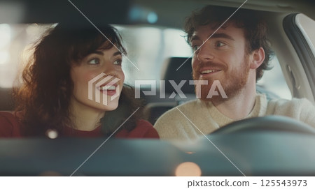 Young couple enjoying the experience of testing a new car, engaging in conversation and smiling while selecting the perfect vehicle to meet their needs in a vibrant dealership showroom 125543973