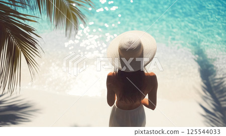 A young elegant woman in big white hat, sunhat back view on a sandy beach in summertime. Summer vacation on ocean shore. Palm trees shadows Calm water This is AI-generated item 125544033