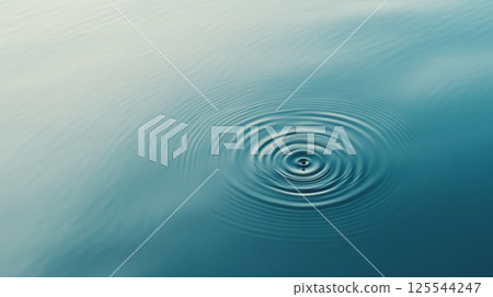 Concentric ripples expanding outwards from the point of impact of a single water droplet, creating a mesmerizing pattern on a calm, blue water surface, evoking tranquility and mindfulness 125544247