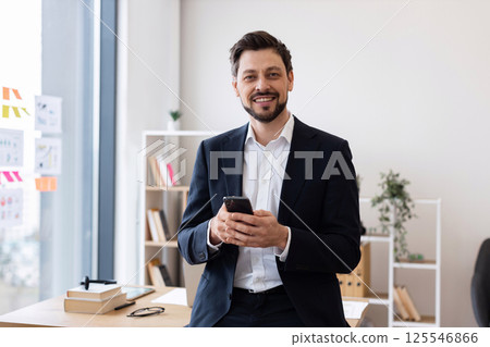 Adult male business professional interacting with smartphone in bright office with window view. Adult male business professional interacting with smartphone in bright office with window view. 125546866