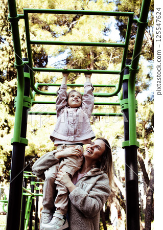 little cute girl with her mother and twin sister having fun on training playground outside little cute girl with her mother and twin sister having fun on training playground outside 125547624