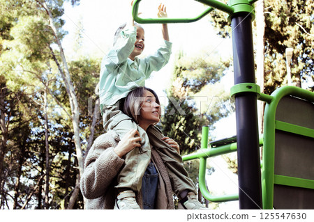 little cute girl with her mother and twin sister having fun on training playground outside little cute girl with her mother and twin sister having fun on training playground outside 125547630