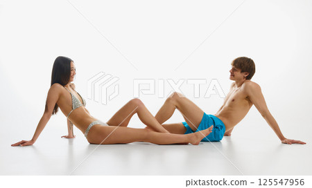 Happy, loving, smiling young man and woman, both in swimwear posing against white studio background. Happy, loving, smiling young man and woman, both in swimwear posing against white studio background. 125547956