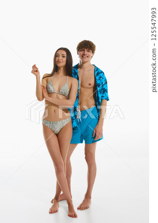 Full-length portrait of elegant young couple, man in tropical beach wear and woman in elegant swimsuit posing against white studio background 125547993