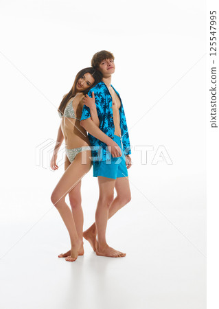 Happy young couple, man in tropical beach wear and beautiful woman in elegant swimsuit posing together against white studio background 125547995