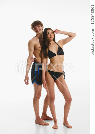 Beautiful young couple, man and woman fit fit, tanned bodies, posing in beachwear together against white studio background. Beautiful young couple, man and woman fit fit, tanned bodies, posing in beachwear together against white studio background. 125548001
