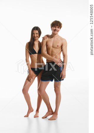 Full-length portrait of confident handsome young man and beautiful smiling woman, posing in beachwear against white studio background Full-length portrait of confident handsome young man and beautiful smiling woman, posing in beachwear against white studio background 125548005