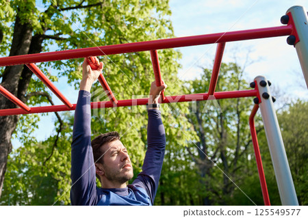 Man training on monkey bars in outdoor fitness park Man training on monkey bars in outdoor fitness park 125549577