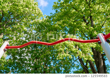 Curved outdoor horizontal bar for pull-ups in park with green trees and blue sky 125549583