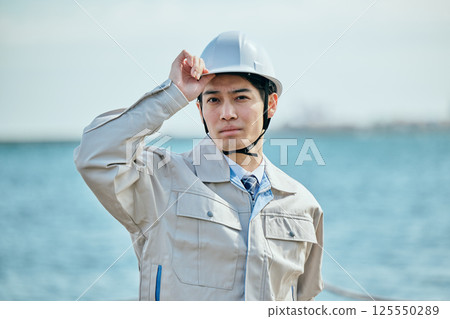 A young man in his 20s wearing work clothes and a helmet 125550289