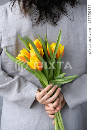 woman holds bouquet of yellow-red tulips in hands. birthday or mother's day gift. view from back. 125550553