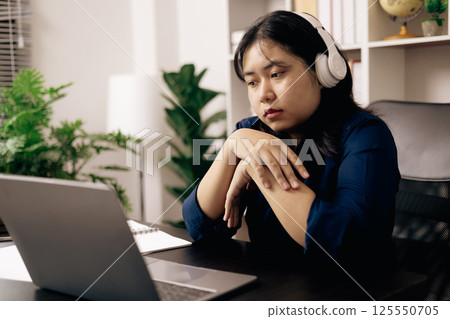 creative young student uses a laptop to complete online homework for college and university courses. Woman studies a book and conducts research for online academy using laptop in office. 125550705
