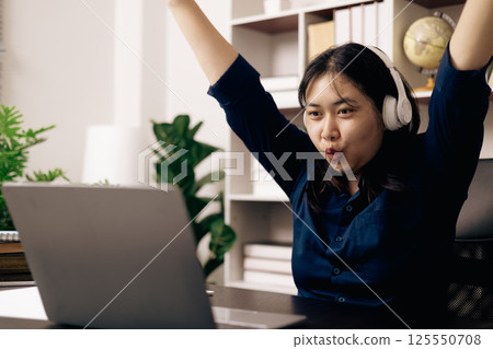 Happy student, studying for MBA exam, takes advantage of distance learning to attend school from home, balancing training and class. Woman studies book and research for online academy using laptop. 125550708