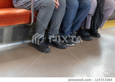 The foot area of three people sitting on train seats, long bench-style chairs The foot area of three people sitting on train seats, long bench-style chairs 125551064