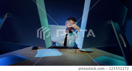 Frustrated businessman sitting in office, reading financial reports during severe collapse, working overtime under pressure. Frustrated businessman sitting in office, reading financial reports during severe collapse, working overtime under pressure. 125552272