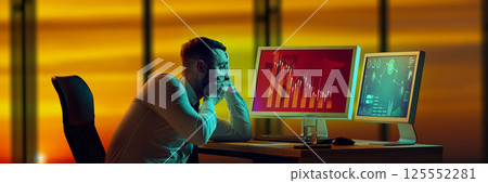 Shocked businessman staring at desk, looking at monitors showing collapsing financial charts, total economic collapse. 125552281